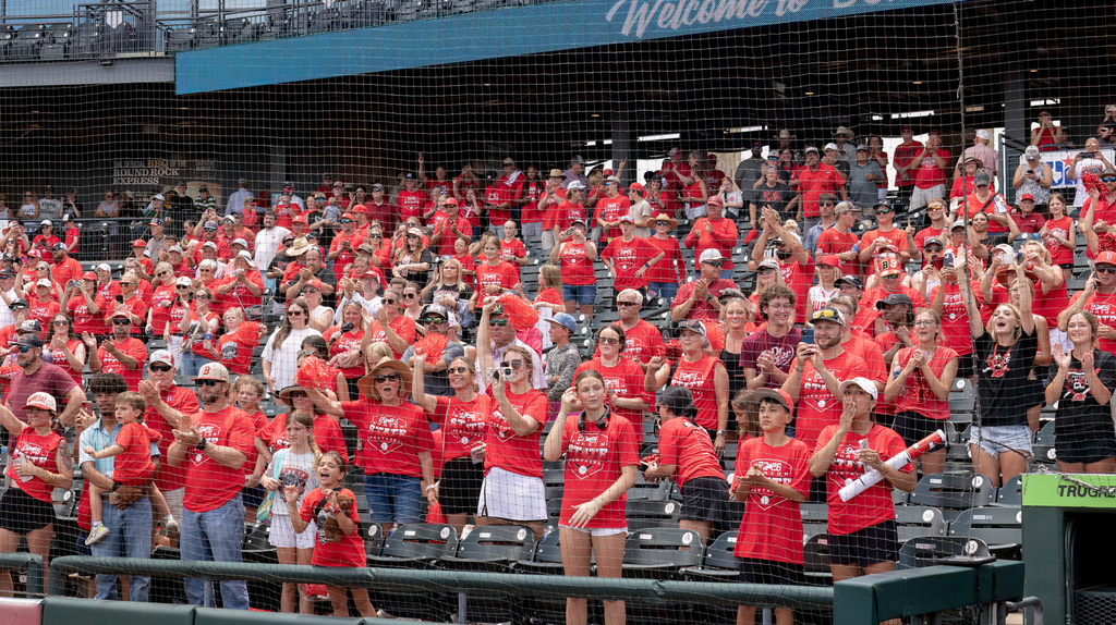 stadium stands full of people of different ages and races wearing red hats and t-shirts appearing to cheer