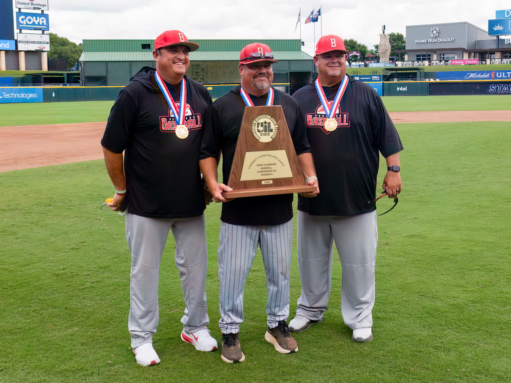 Three men dressed in black shirts and white pants standing on a baseball field.  middle man is holding the UIL baseball trophy.