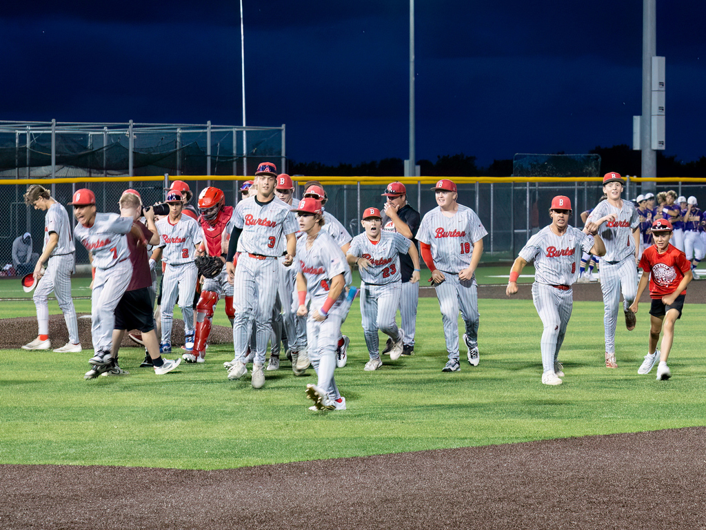 group of high school boys in gray uniforms and red hats appearing to walk and start to run across a baseball field.