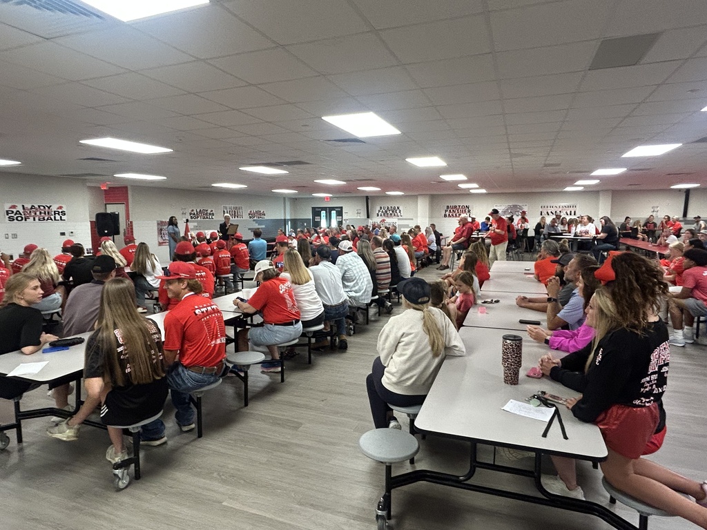 community members look on as 2 women speak at the front of a cafeteria