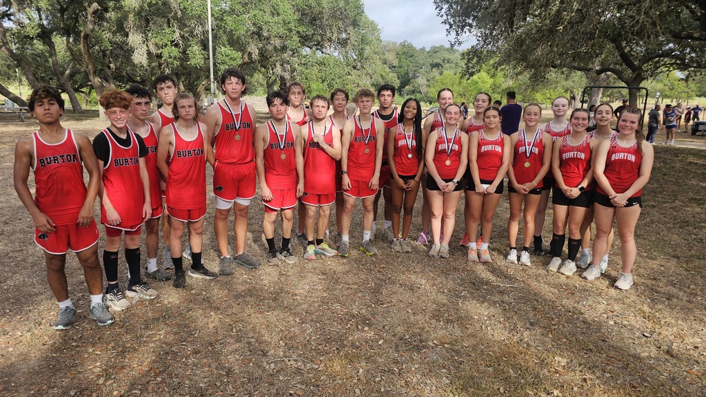 Group of boys and girls standing outside under trees. They are wearing red shorts and tank tops and smiling at the camera.