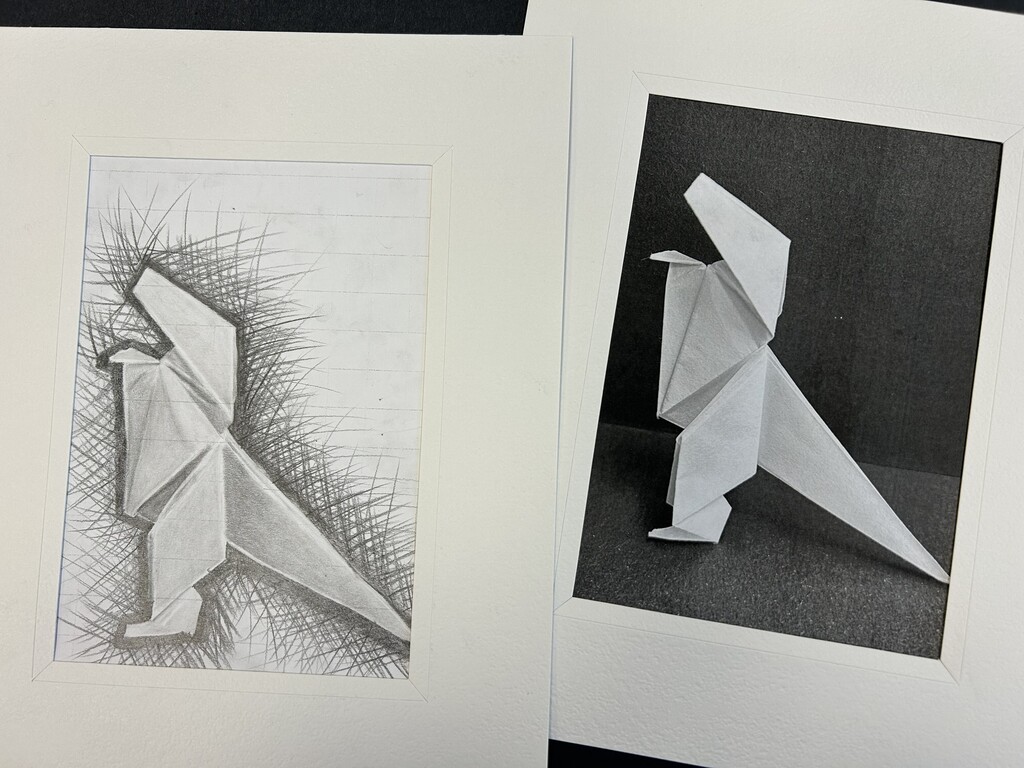 Two framed artworks displayed side by side, each depicting a white origami figure resembling a standing bird or abstract animal. The left artwork is a pencil drawing of the folded-paper figure against a textured, grassy background; the right is a photograph of the three-dimensional origami figure against a dark background.