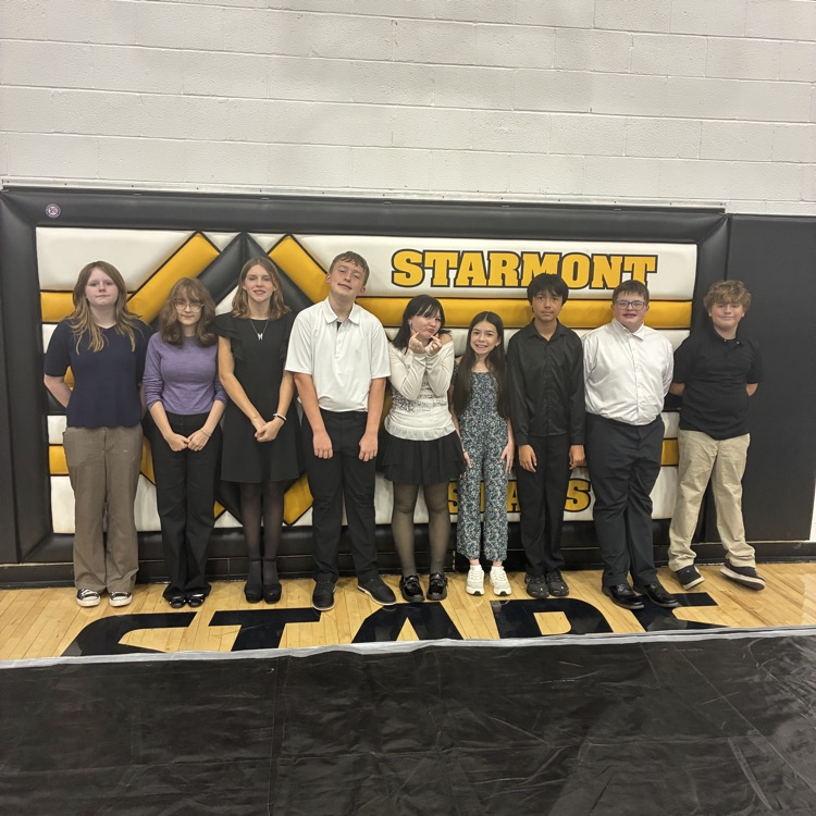 Nine junior high band students are lined up against a wall, smiling for the camera
