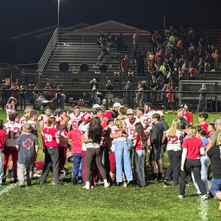 football team celebrate on the field in a circle. fans join on the field to celebrate the win
