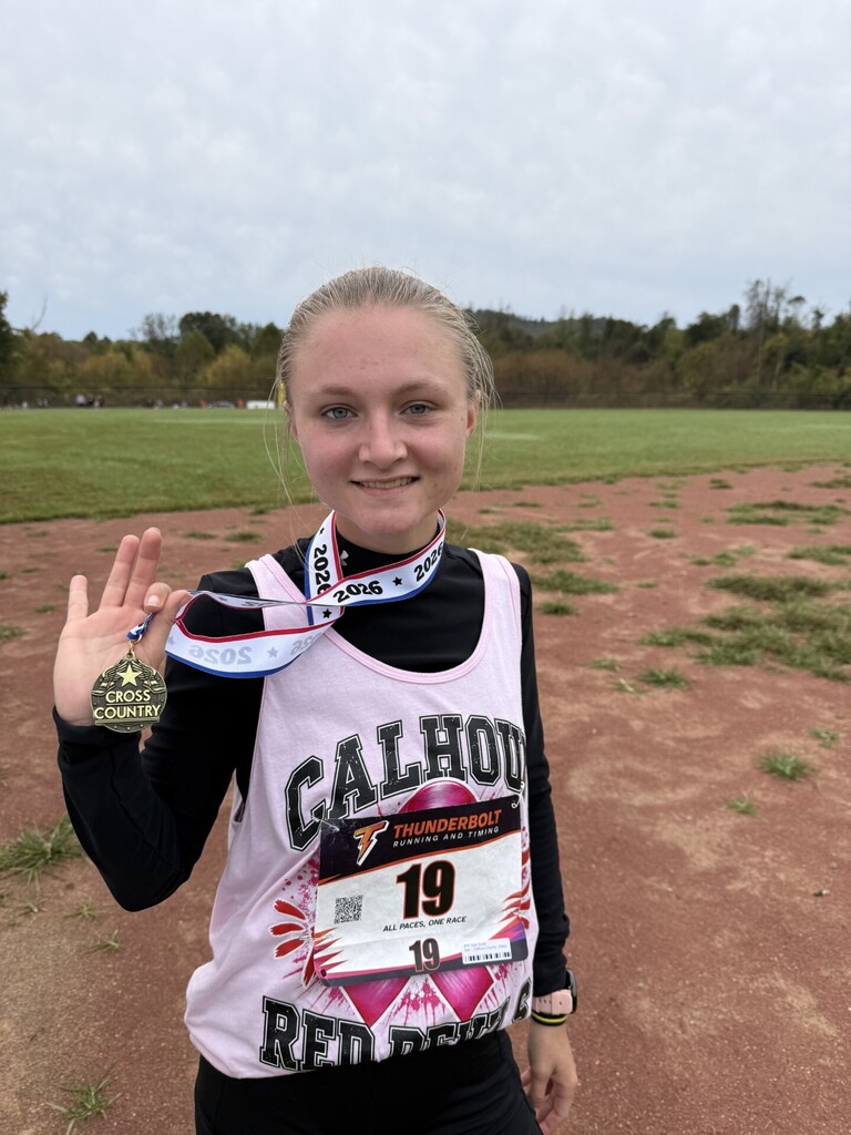 Hs Girl stands showing her medal in her right hand.