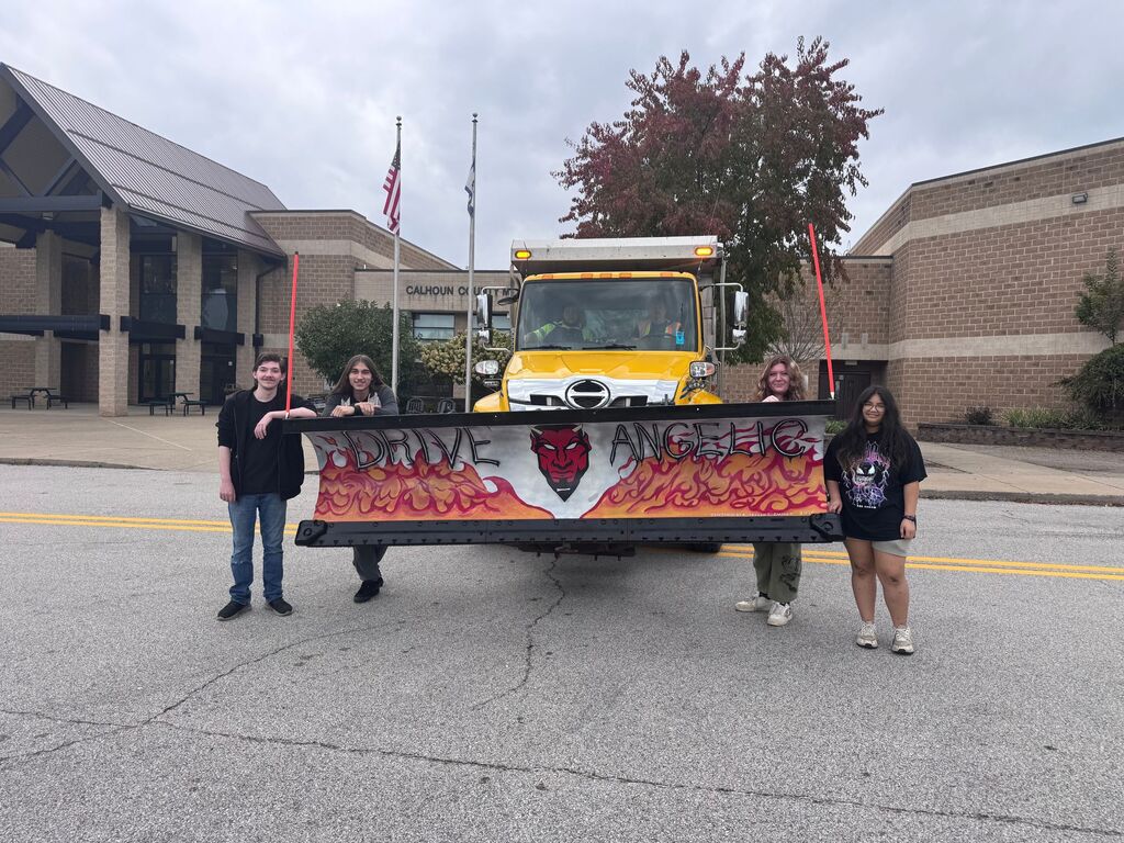 Student stand with snow plow truck with a design they painted on the front of the truck. 