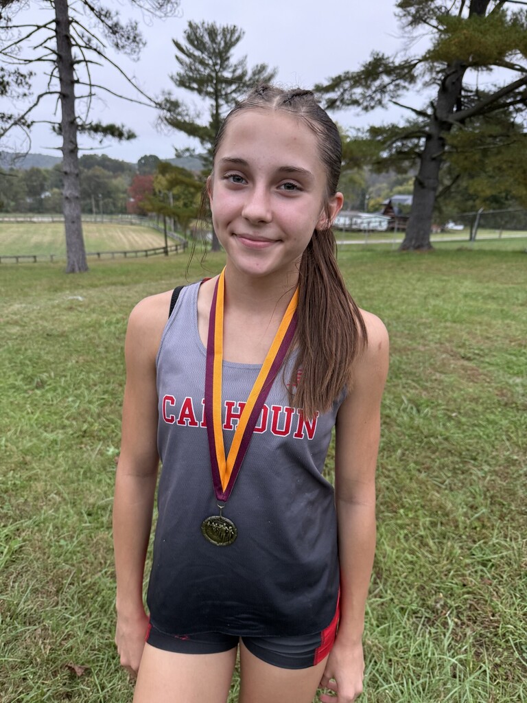 5th place Brook Tingler stands with medal around her neck with a field behind her. 