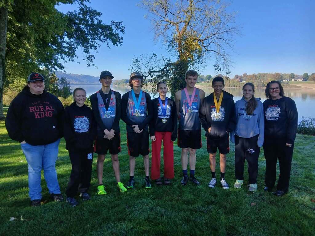 Coachs stand on each side of the HS XC team with river in bacground