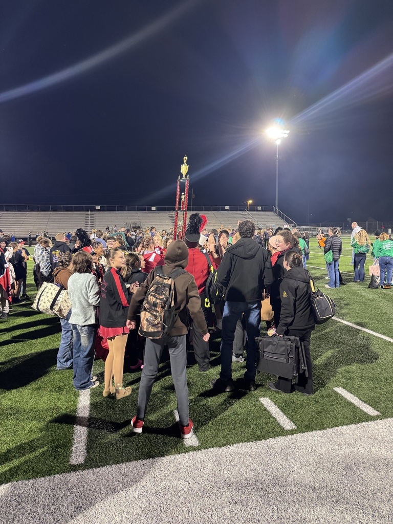 Tropy lifted in air while students stand in circle around it on green football turf