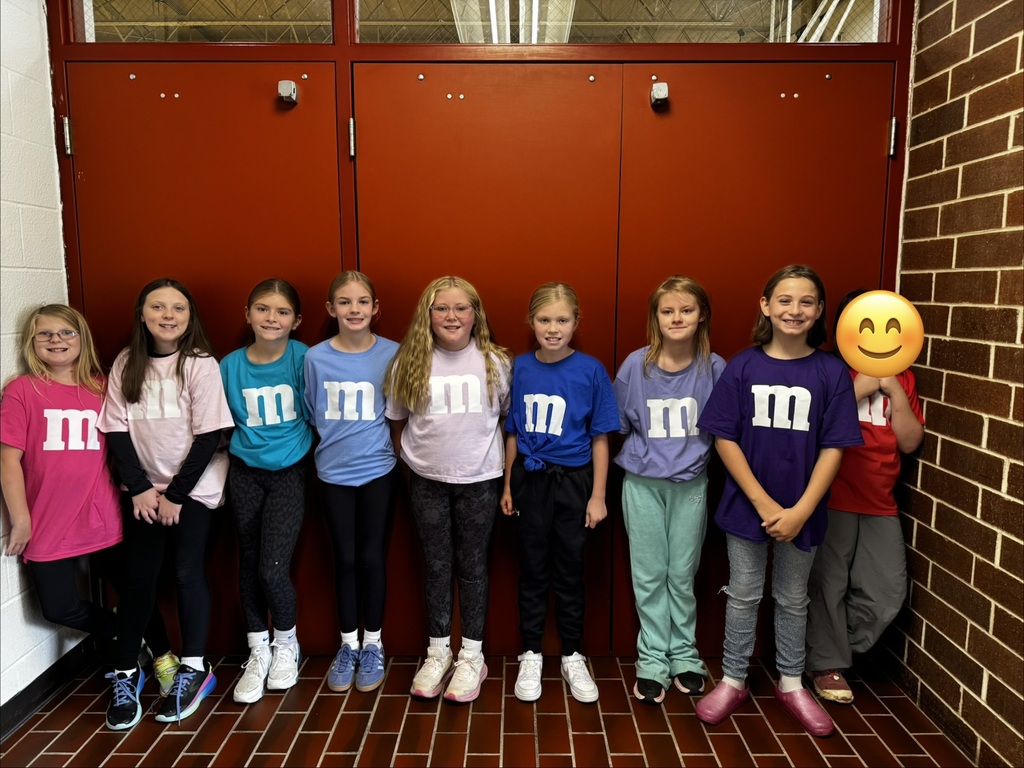 Students against wall showing off their M&M tee-shirts