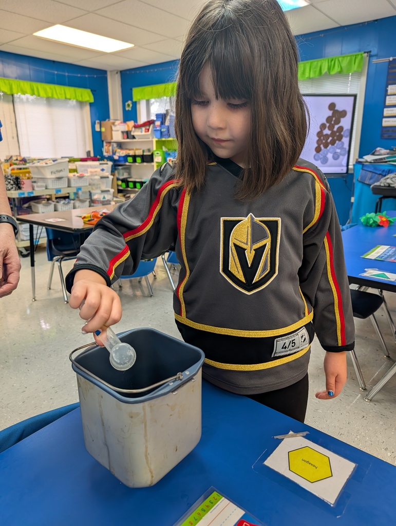 Student pouring ingredients into canister on a desk in classroom. Making bread. Teacher assisting.