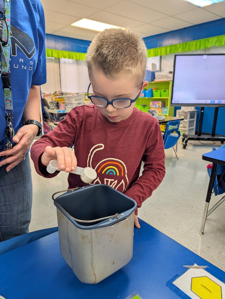 Student pouring ingredients into canister on a desk in classroom. Making bread. Teacher assisting.