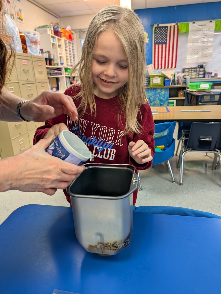 Student pouring water into canister on a desk in classroom. Making bread. Teacher assisting.