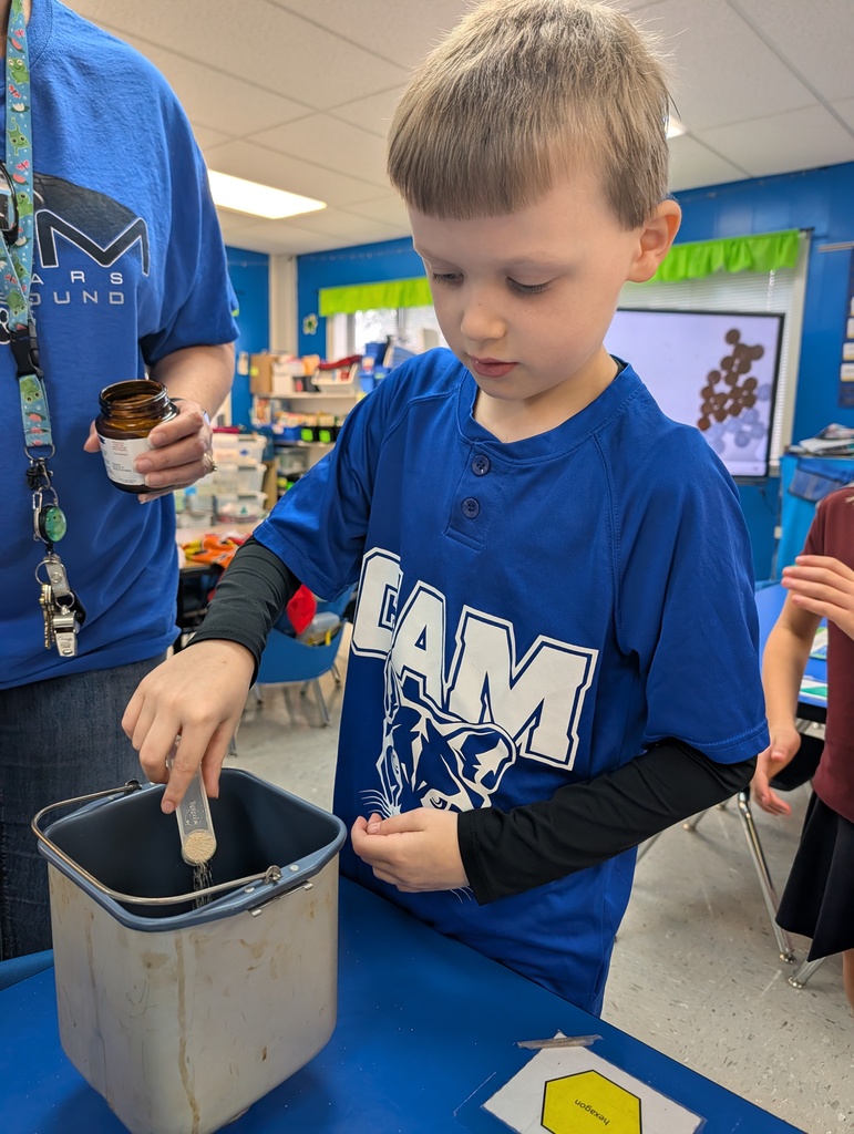 Student pouring ingredients into canister on a desk in classroom. Making bread. Teacher assisting.