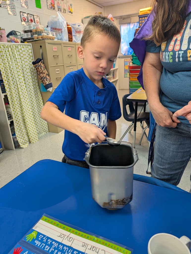 Student pouring ingredients into canister on a desk in classroom. Making bread. Teacher assisting.