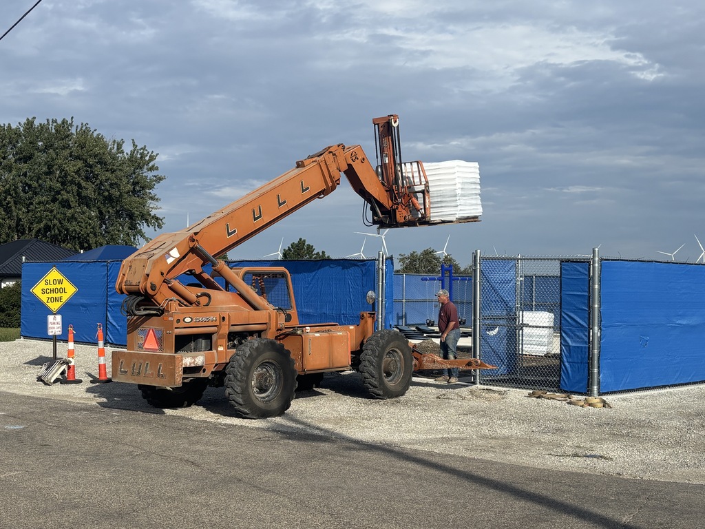 Construction vehicle lifting items for new playground over a fence.