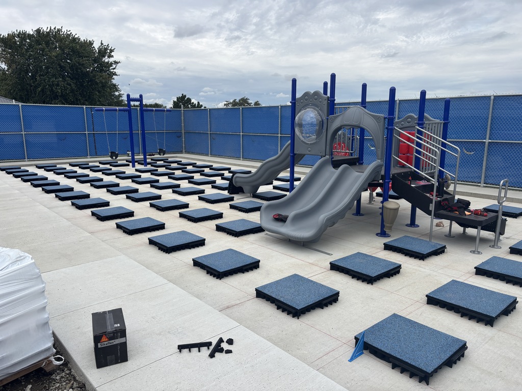 Inside the Elementary new playground fenced off area. Some of the playground has been built with blue pads all around on the ground.