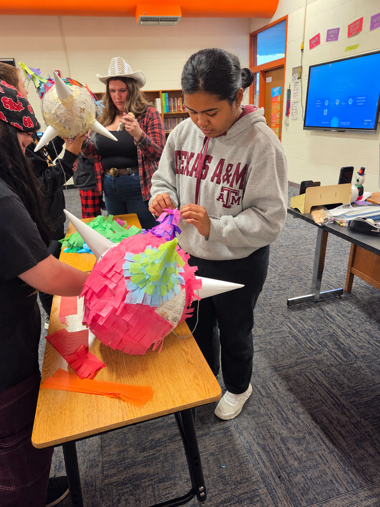 Students decorate handmade piñatas with colorful tissue paper, adding purple fringe to a pink piñata.