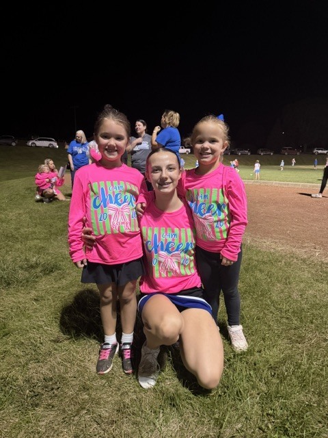 Cheer leaders in neon pink shirt smiling with 2 youth cheerleaders