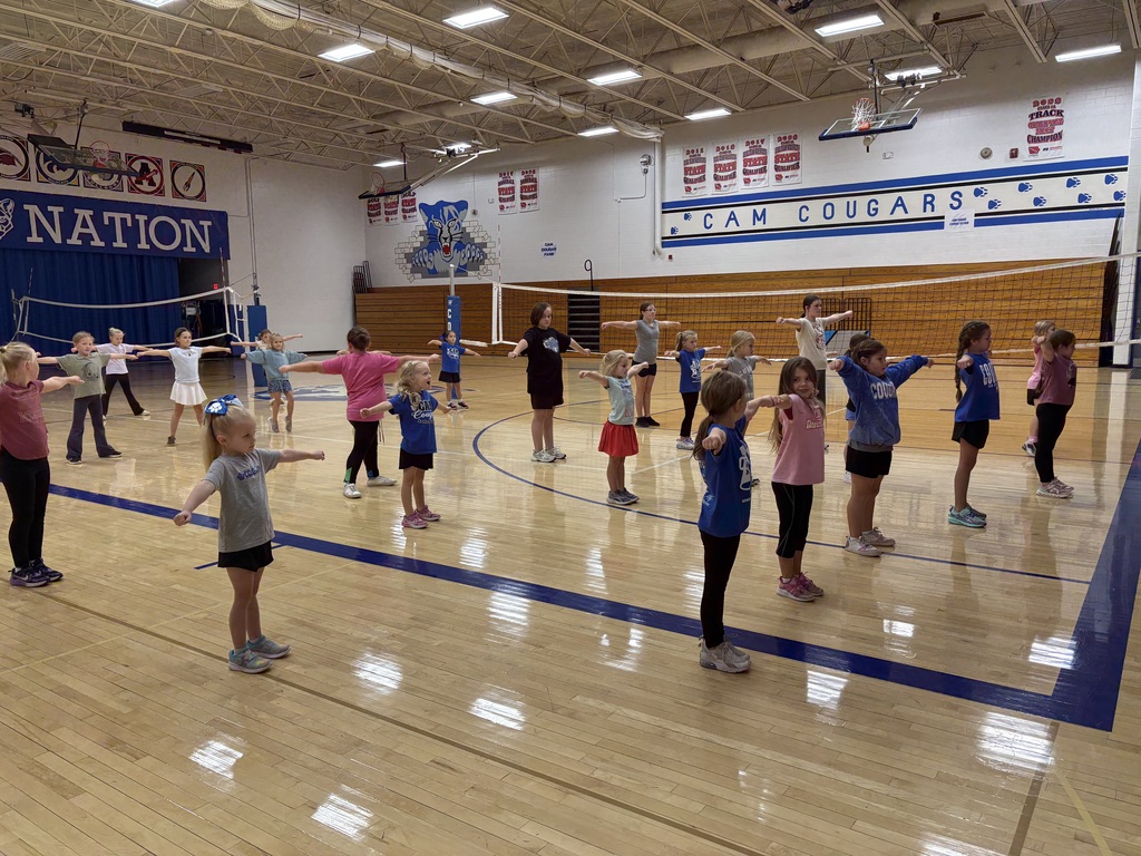 Youth cheerleaders spread out in the gym with their arms out in a T position