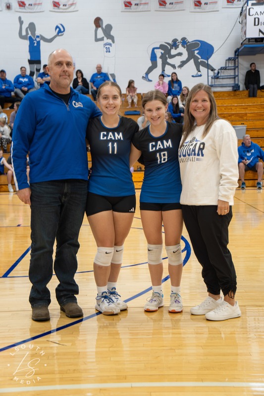 Two CAM volleyball seniors pose with two family members on the gym court.