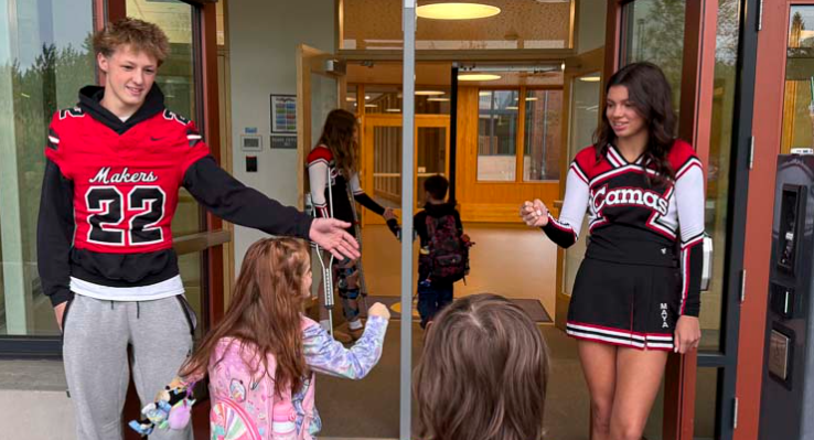 A football player and cheerleader greeting elementary students