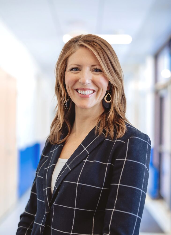 A school staff member smiles while posing for a professional portrait in a hallway.