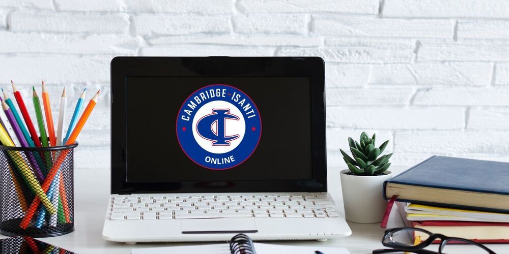 Laptop on a desk showing the Cambridge-Isanti Online logo on screen, surrounded by school supplies.