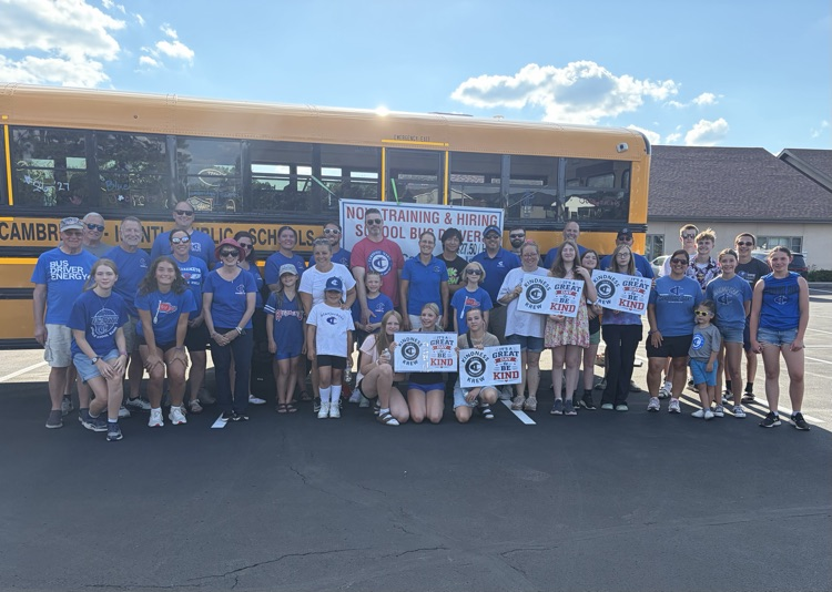 A group of smiling school staff and volunteers standing in front of a school bus preparing to walk in a community parade