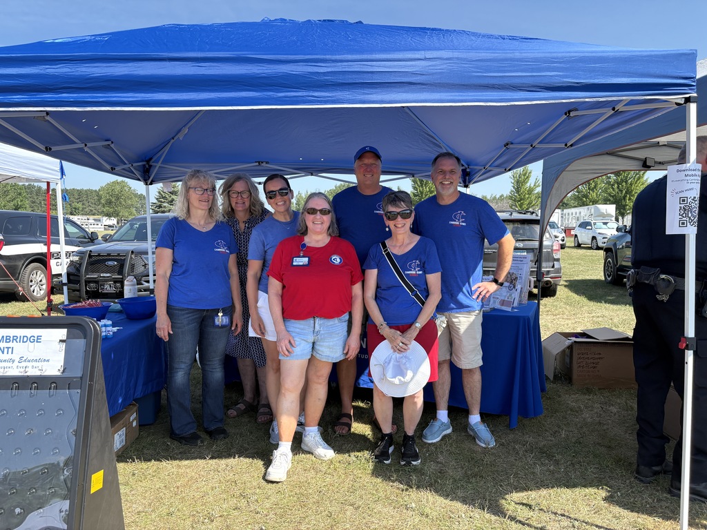 Staff stand together under a blue canopy at the Isanti County Fair Kids Day event, welcoming families at the district's community booth.
