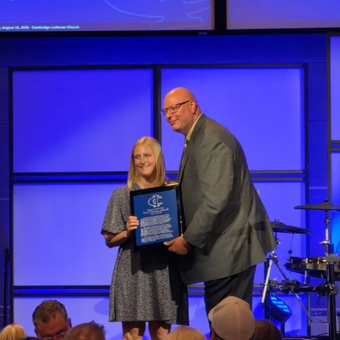 A school official presents an award plaque to a recipient on stage at the Bluejacket Hall of Fame event.
