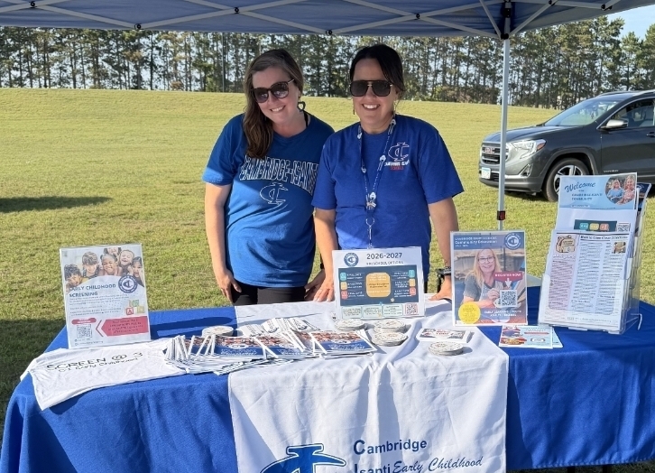 Early learning administrators smiling under a canopy at a an event in the park. 