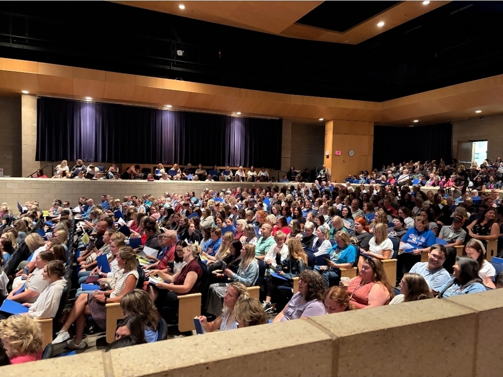 A large audience is seated in a theater, attending a presentation.