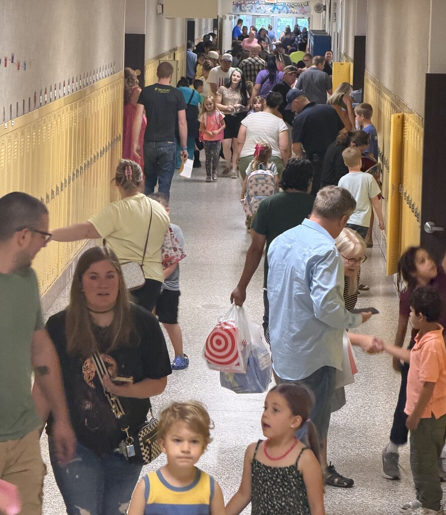 Students and families walk down a crowded school hallway lined with yellow lockers during an open house event.