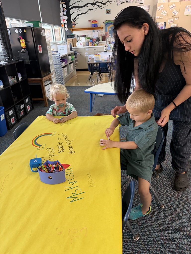 Young boy writing his name on a large piece of paper with mom watching over his shoulder