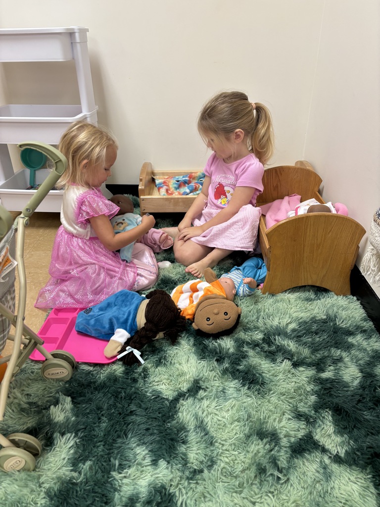 Two young girls taking care of their dolls in the housekeeping area