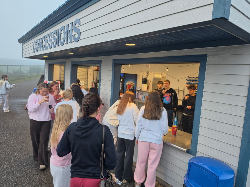 Students line up to buy snacks at a school concessions stand window.
