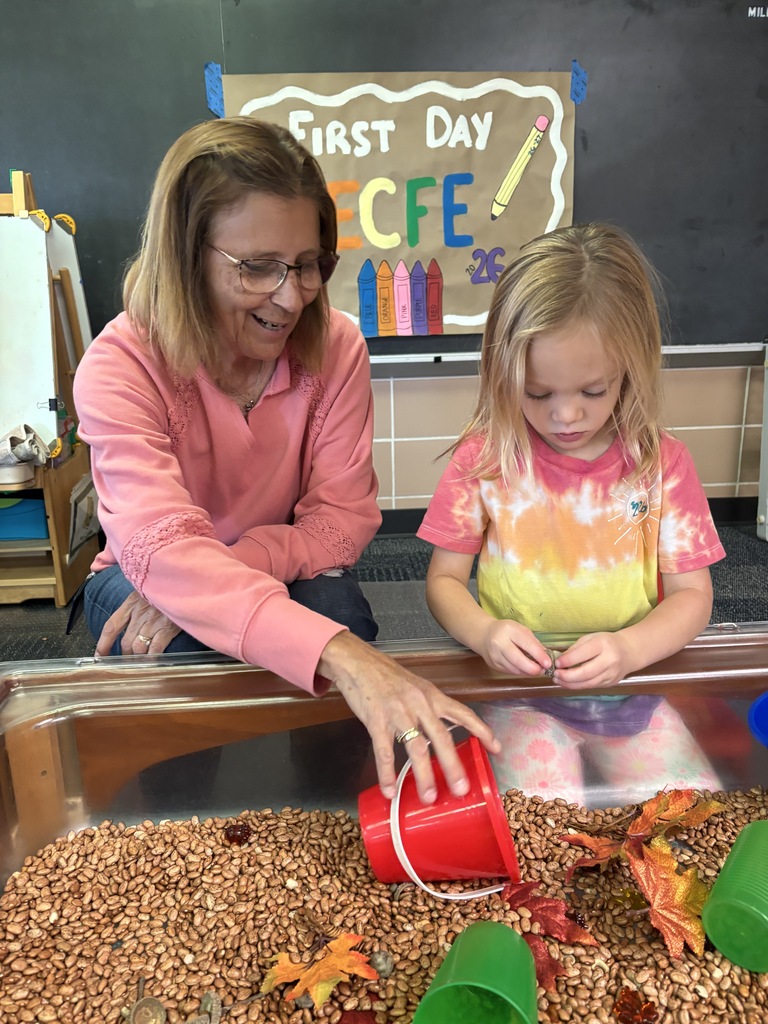 A teacher and a young student play in a fall-themed sensory bin filled with beans and leaves under a "First Day ECFE" sign.