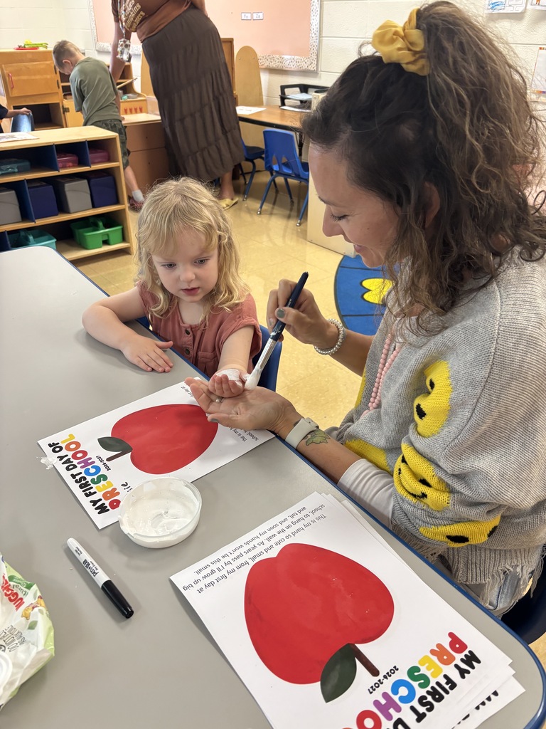 A teacher paints a preschool student's hand to create a keepsake on her first day of school.