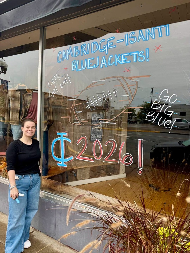 Leader window front. The window is painted for Cambridge-Isanti Homecoming. There is a woman in a black shirt and blue jeans smiling by the display.