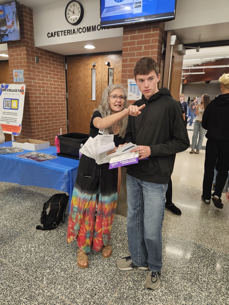 A volunteer points in a direction while handing materials to a student at a high school college fair.