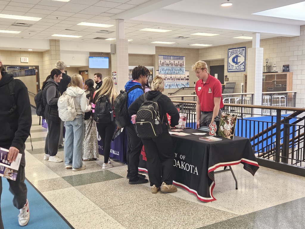 Students gather around University of North Dakota tables during a college fair in a school hallway.