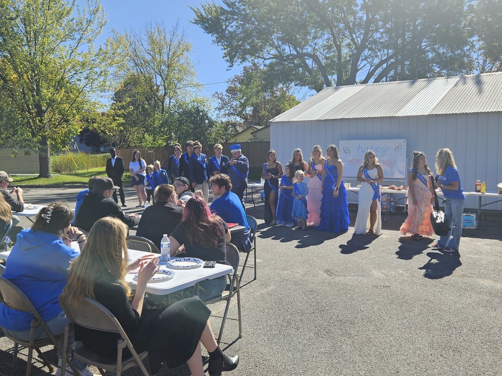 A group of people sitting at a table watching the homecoming court. It is a bright and sunny day. 