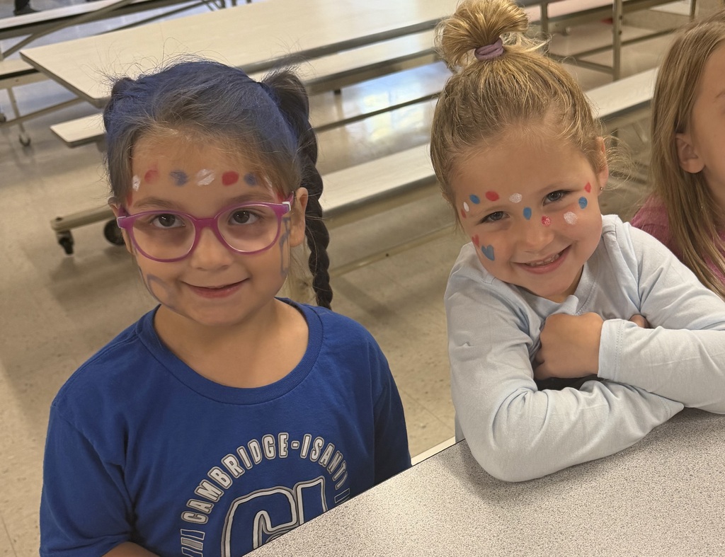 Two students sitting at lunch table smiling with each other in bluejacket spirit clothing and red, white, and blue face makeup. 