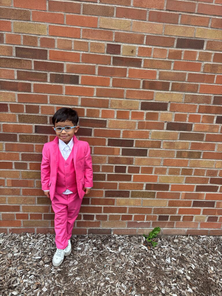 Young boy stands in front of a brick wall in a bright pink tux for "Dress your Best" theme day.
