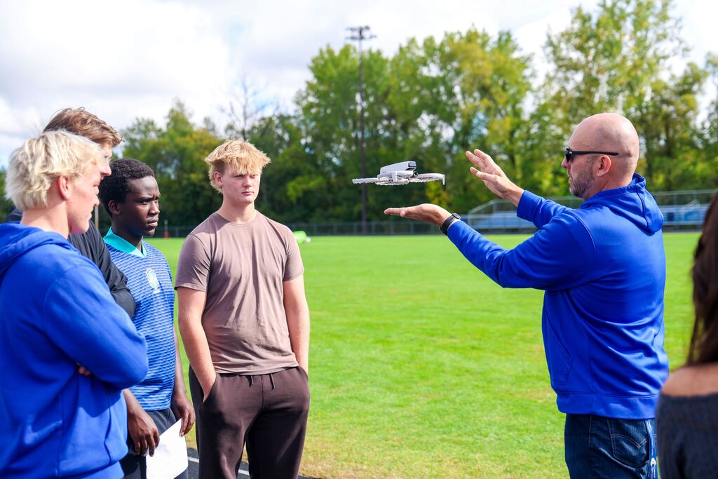A teacher demonstrates a small drone hovering over his palm to a group of interested students.