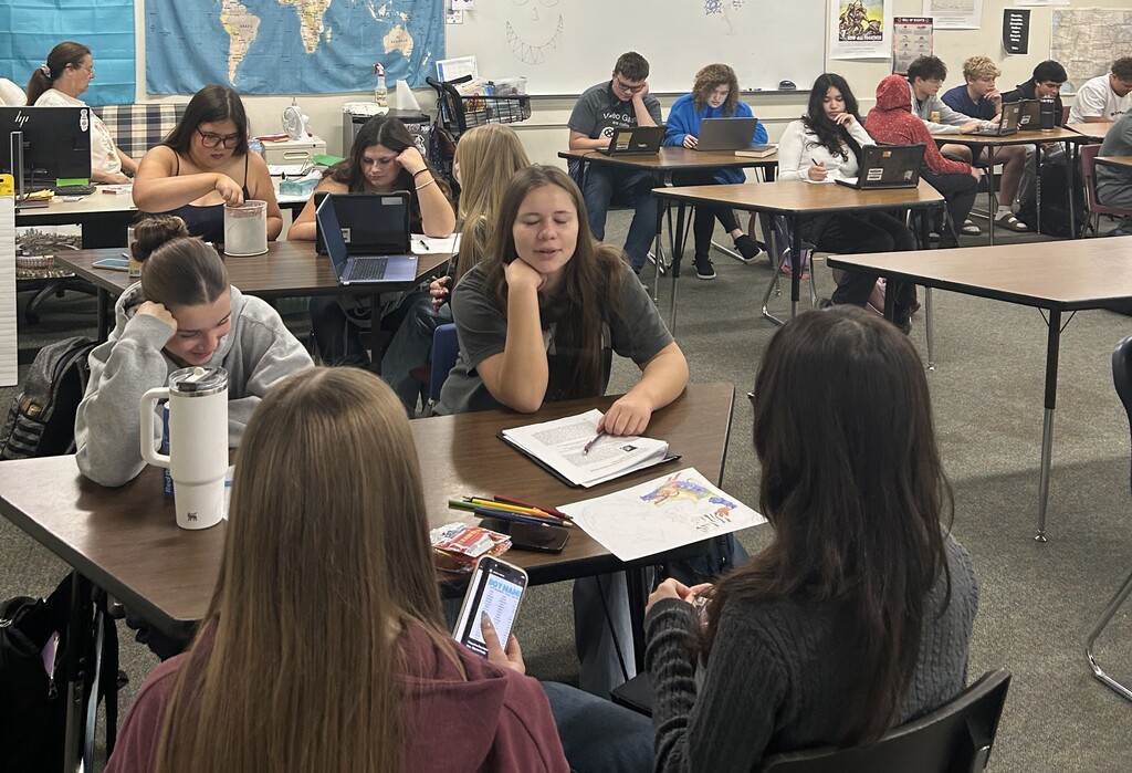 5 tables with groups of students working together on school work and having conversations