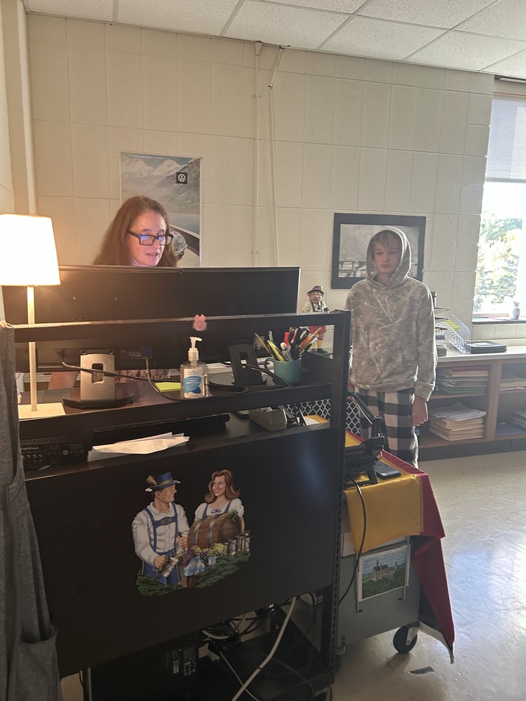 Student stands next to teacher near a computer in a dimly lit room.