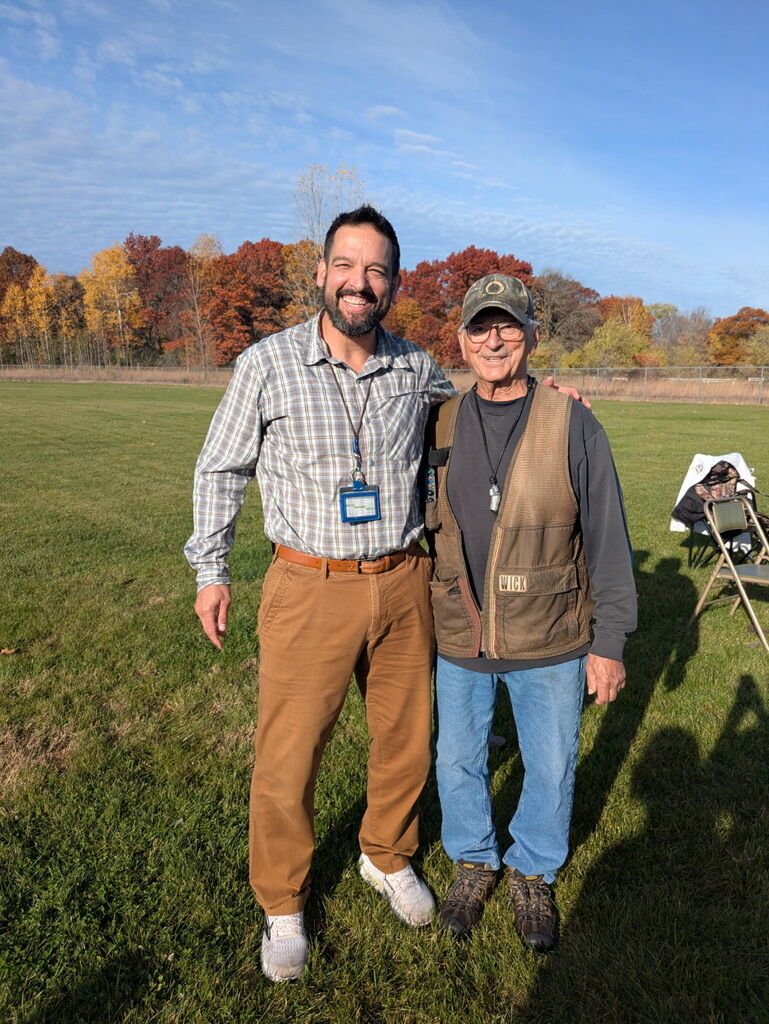 Mr. Fuhol and Mr. Jakovich smile and stand together on a grassy field during an outdoor dog training event.