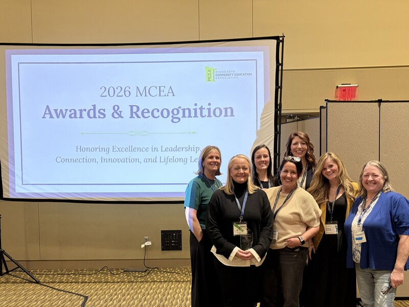 Some members of Cambridge-Isanti Community Education team in front of a presentation slide for the 2026 MCEA Awards & Recognition event.